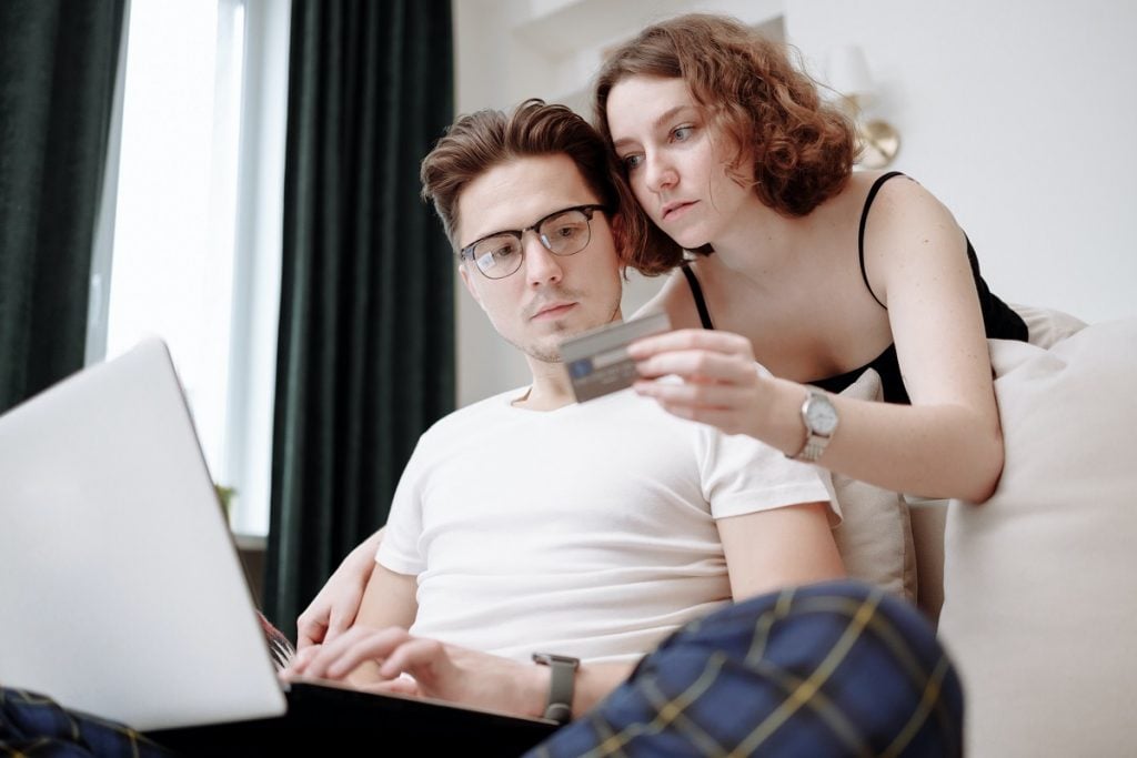 homem mexendo no computador ao lado de mulher segurando cartão de crédito