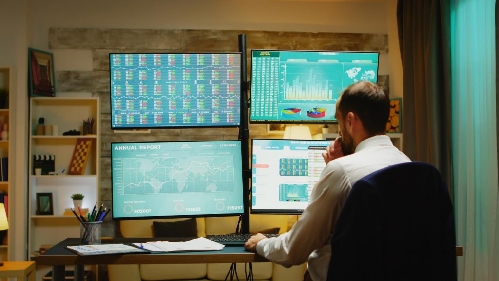 Homem com multiplas telas na sua frente olhando as oscilações do mercado de trader
