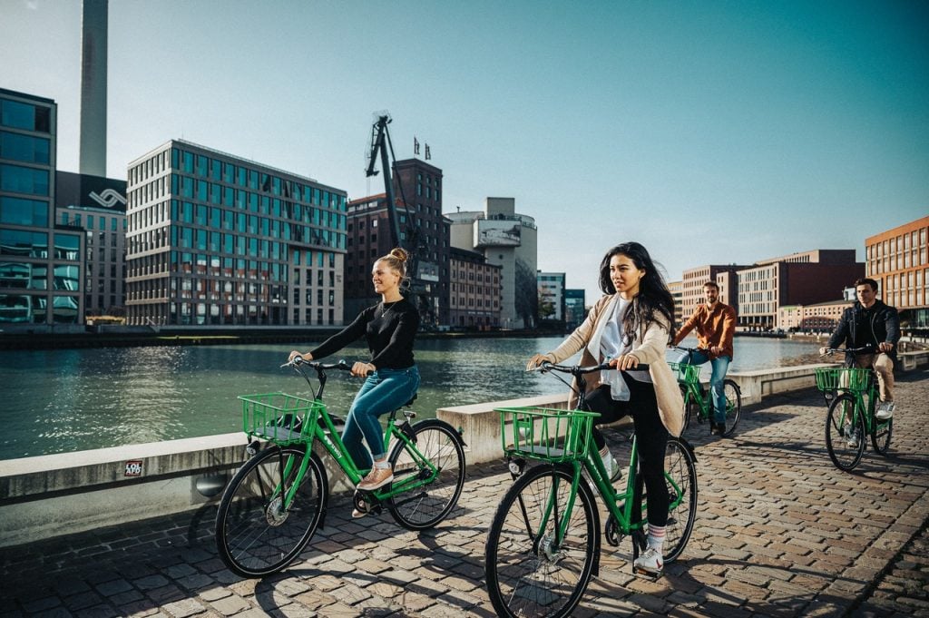 Pessoas andando de bicicleta em área urbana, olhando para frente. Representando o foco em investir em corretoras como a Corretora Bit2me.