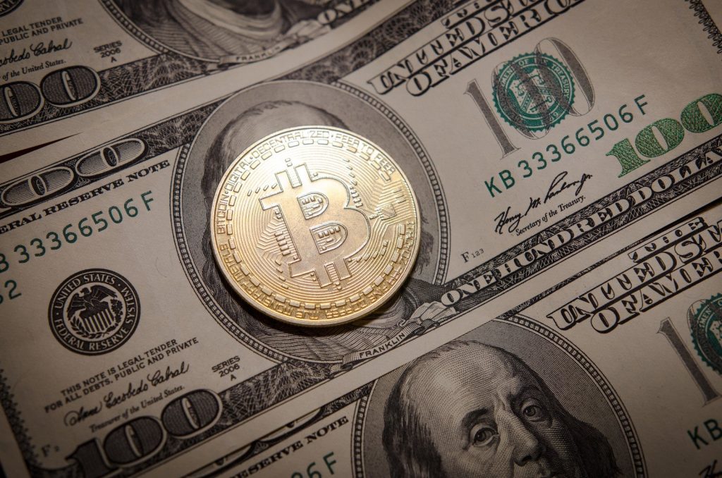 Criptomoeda Bitcoin sobre nota de dólar, Bitcoin é uma das moedas digitais disponíveis para transação na corretora Libertex