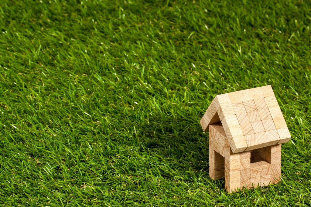 Miniatura de casa feita em madeira, sobre grama, representando o uso do crédito pessoal Creditas para compra de imóvel