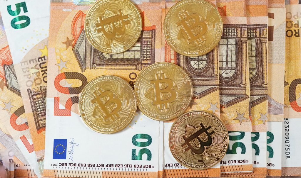 Dinheiro em notas de 50, junto com moedas de bitcoin, simbolizando aderir à corretora BitPreço