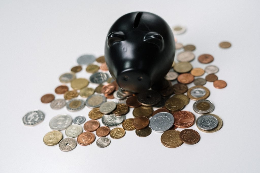 Cofrinho preto de porquinho, com várias moedas ao redor. Representando como conseguir empréstimo em Portugal.