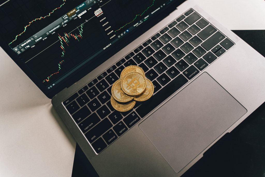 Bitcoins sobre teclado de notebook, na tela é possível ver gráficos de Crypto FX simbolizando investimento com o Banco Carregosa online