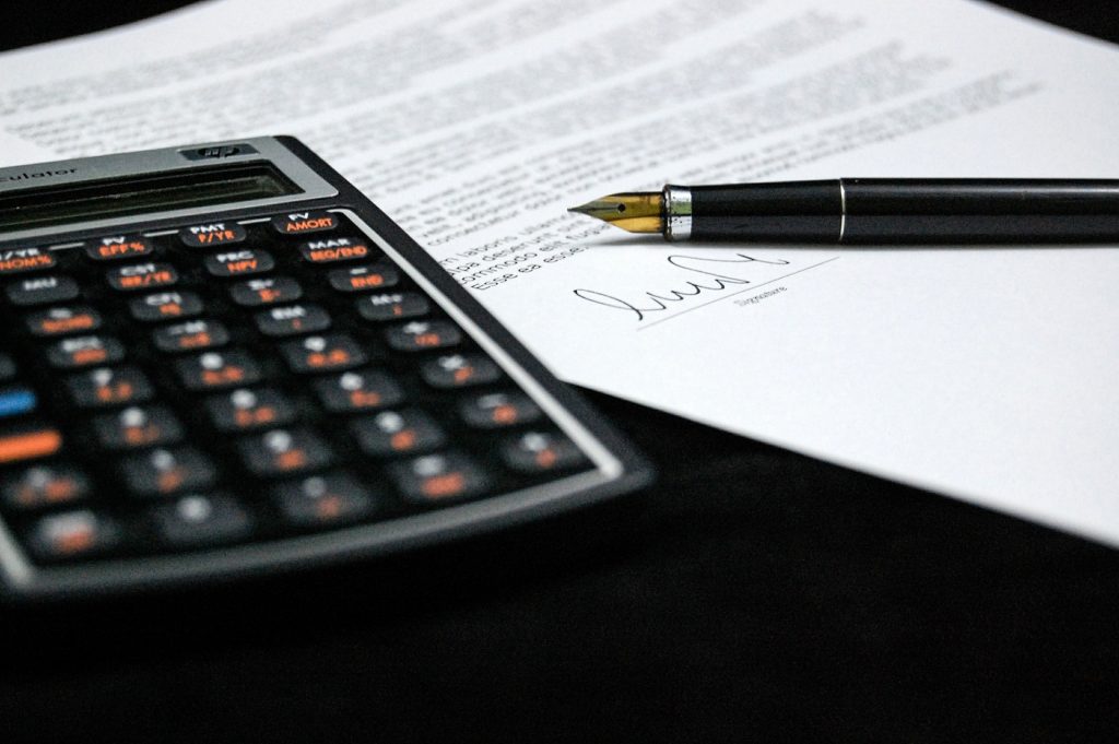 Uma calculadora e um documento assinado, com uma caneta sobre ele.