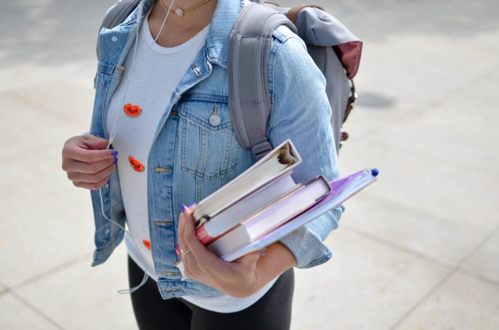 estudante com mochila nas costas e livros e cadernos na mão