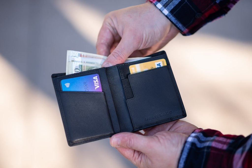 imagem com uma pessoa segurando uma carteira com algumas notas e cartões de crédito
