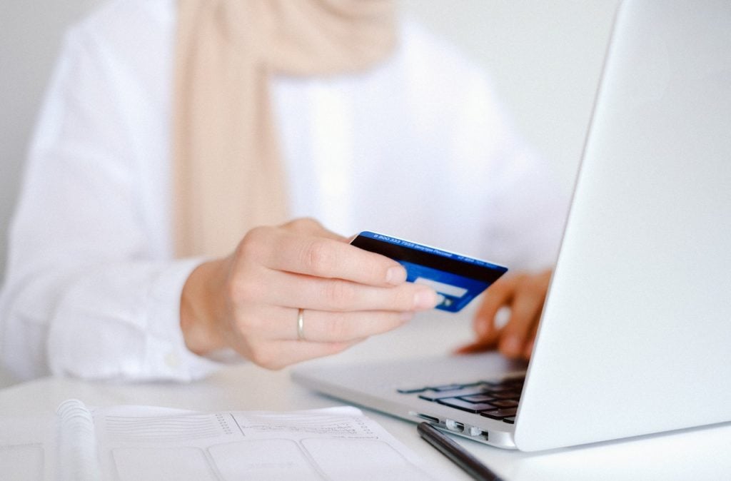 imagem com uma mulher segurando um cartão de crédito em frente a um computador vendo o programa de pontos unibanco