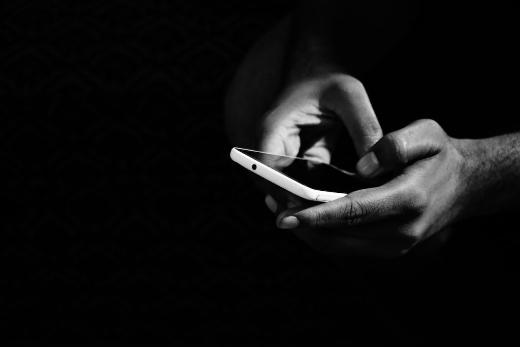 imagem com fundo escuro com uma pessoa com celular na mão pesquisando para conhecer a max finance