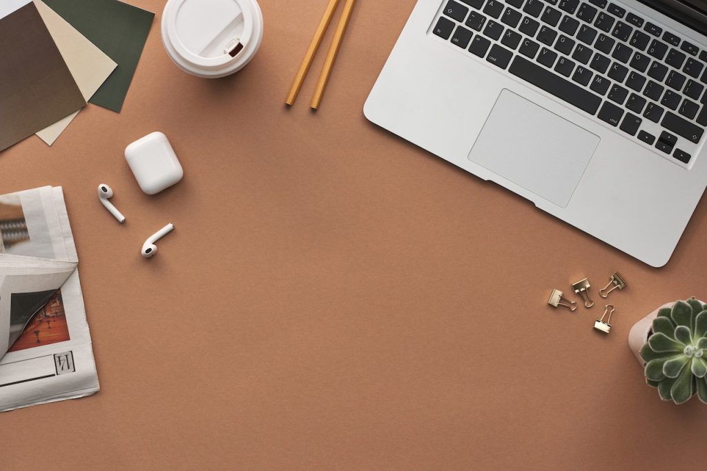 imagem de uma mesa com um notebook, uma xícara de café, fone de ouvido e dois lápis