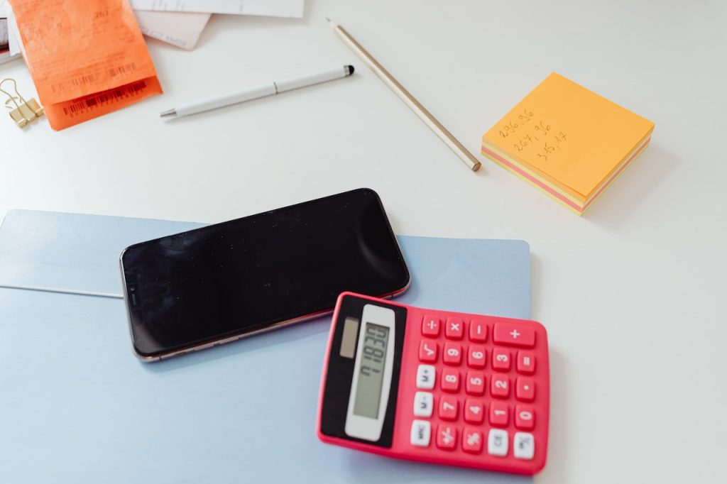 imagem com uma calculadora, celular e alguns papéis sobre a mesa