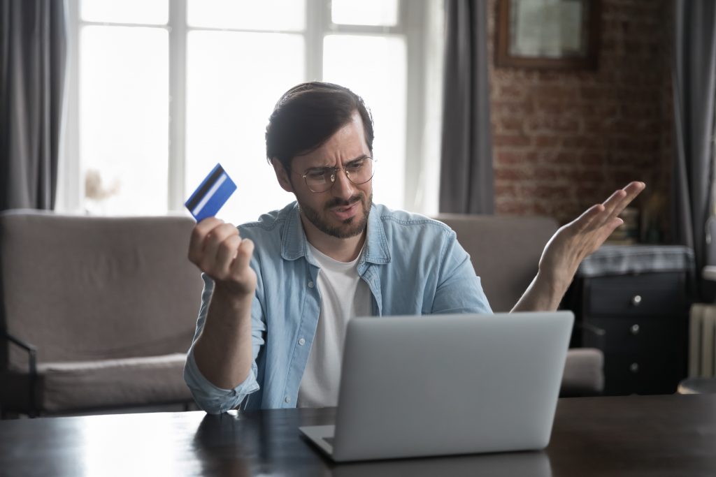 Homem frustrado segurando cartão de crédito e olhando para notebook