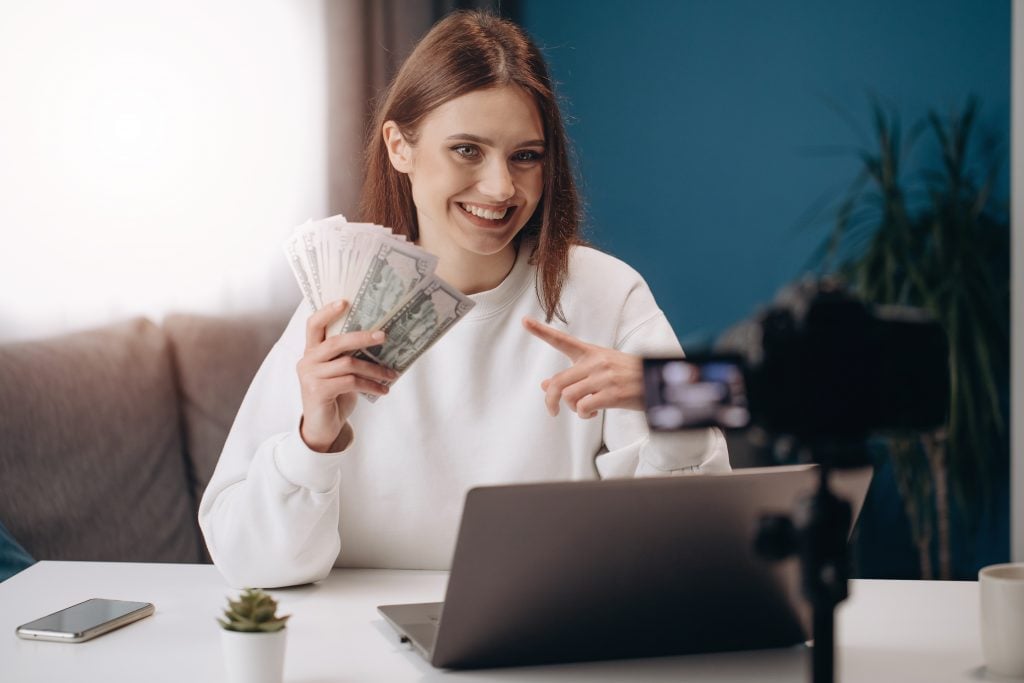 Mulher sorrindo para câmera apontando dinheiro