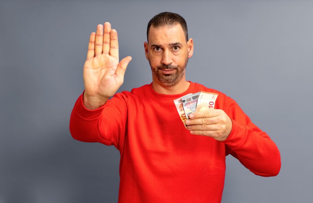 Homem sério segurando euros e fazendo sinal de "pare" com a mão