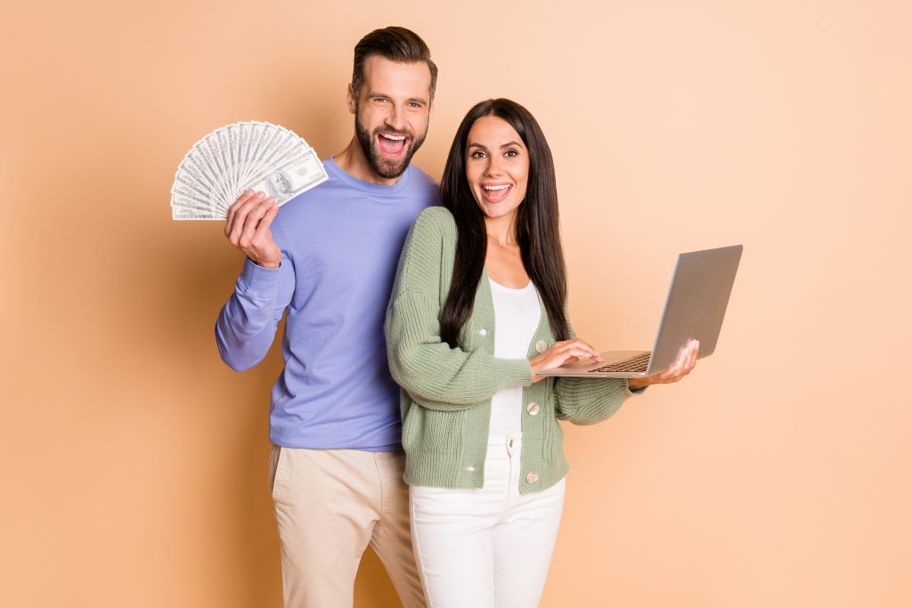 Photo of optimistic couple hold laptop money wear sweater pants isolated on beige color background
