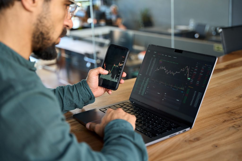 Investor holding phone using laptop analyzing stock trade market data.