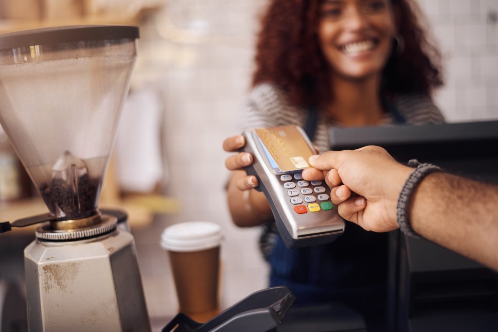 Credit card, nfc and hands of customer in cafe for b2c shopping, point of sale transaction or finance. Closeup, pos machine and contactless payment, rfid and money in coffee shop, restaurant or store