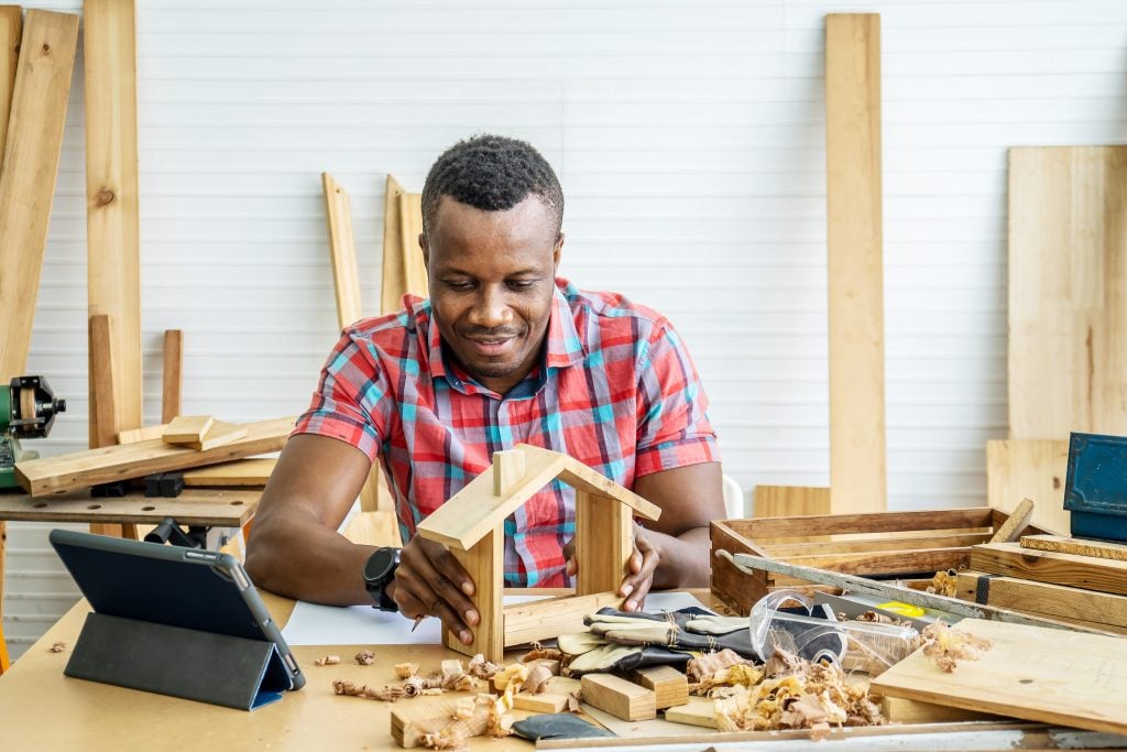 Homem construindo objeto de madeira com tablet ao lado