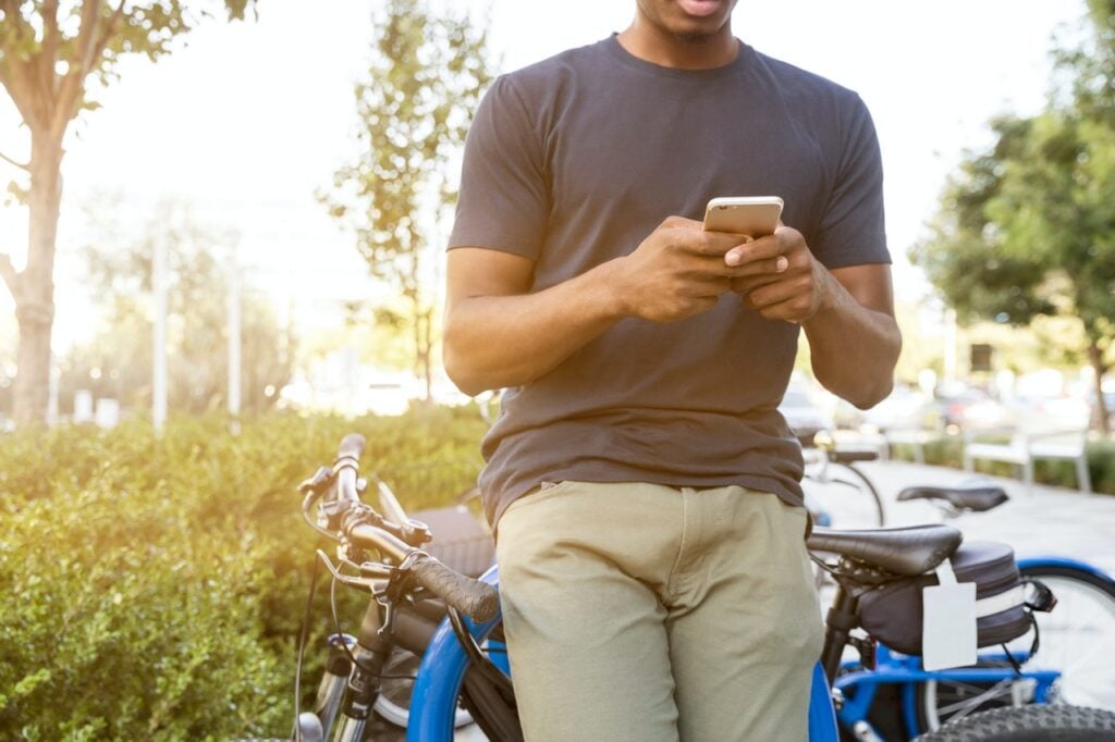 Homem ao ar livre, apoiado em bicicleta, usando o celular
