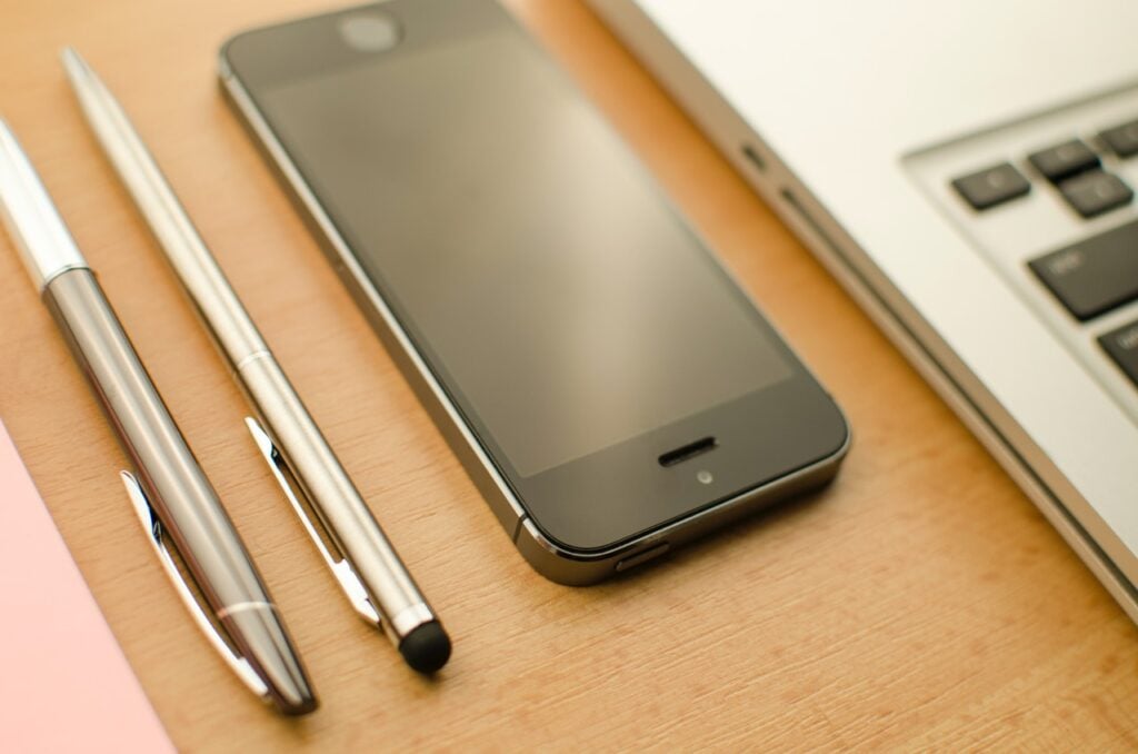 Celular, notebook e canetas sobre a mesa