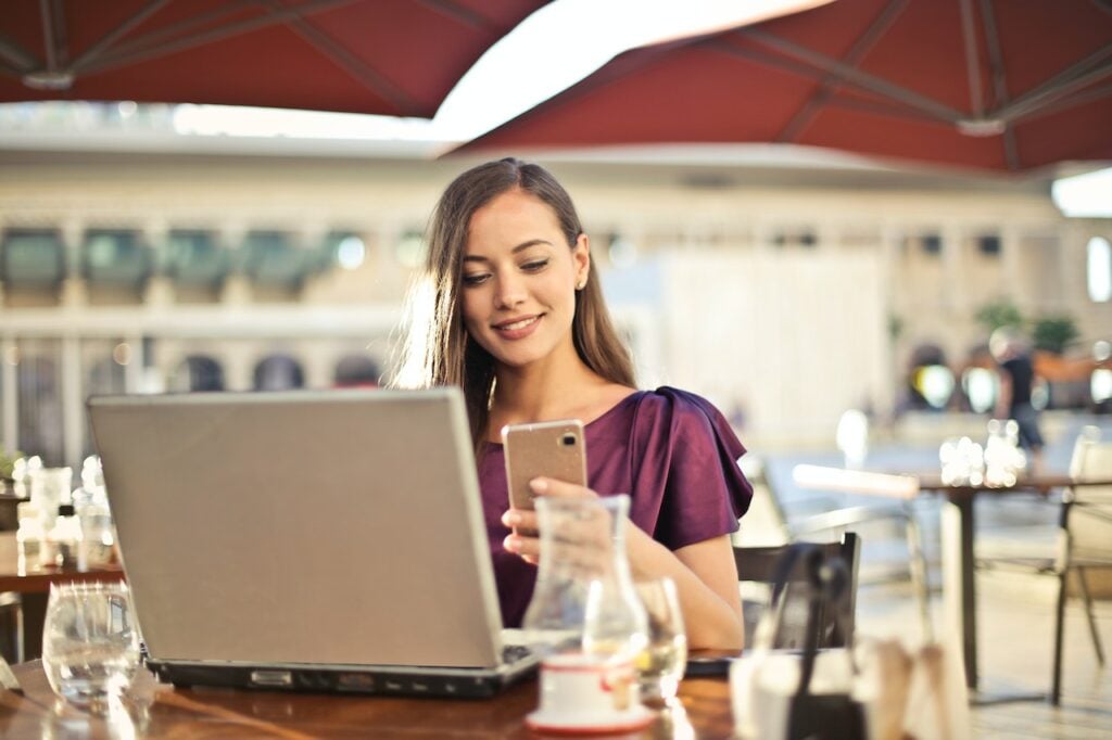 mulher sentada em um café com computador na mesa e celular na mão