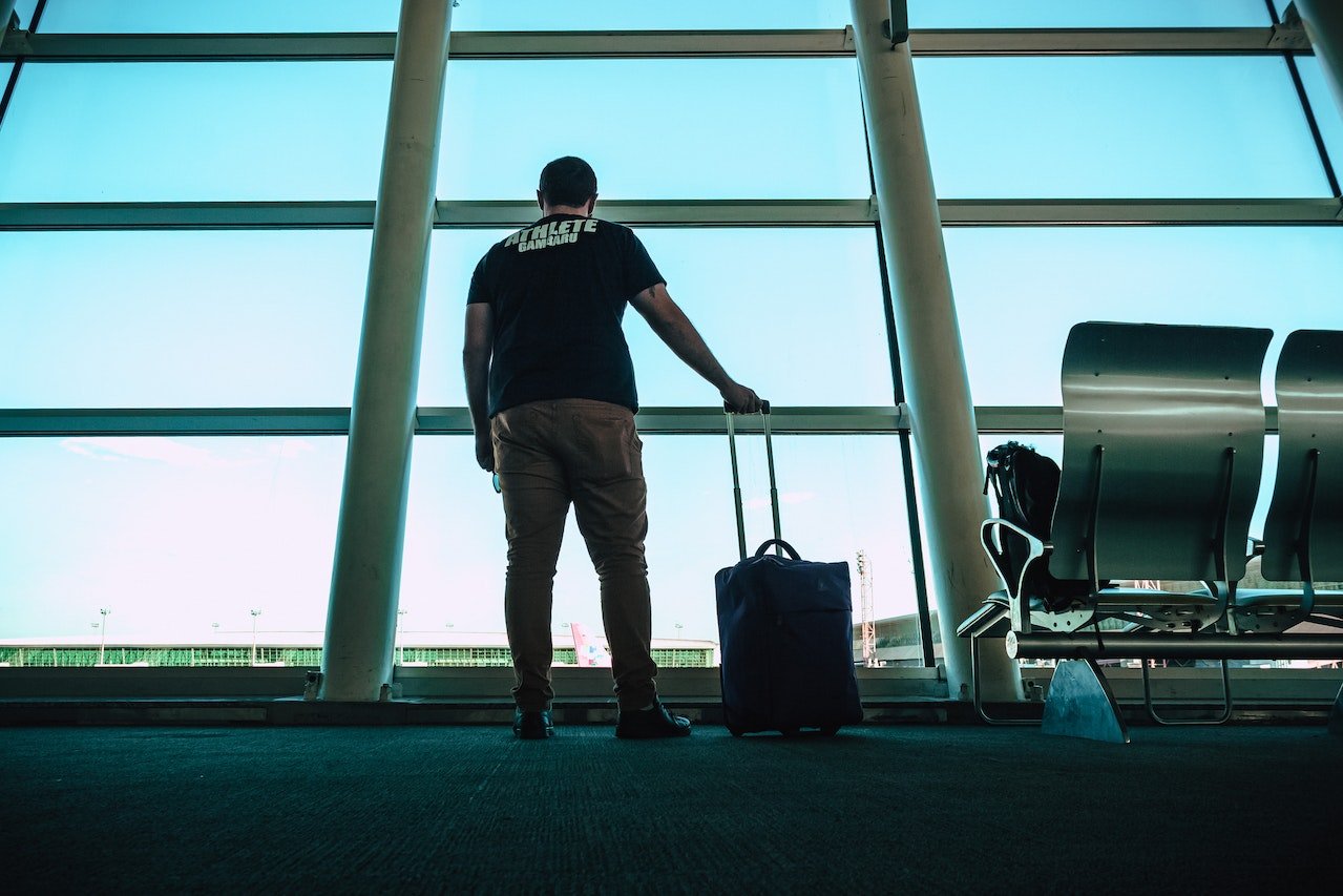homem segurando mala de rodinha e aguardando para embarcar no aeroporto
