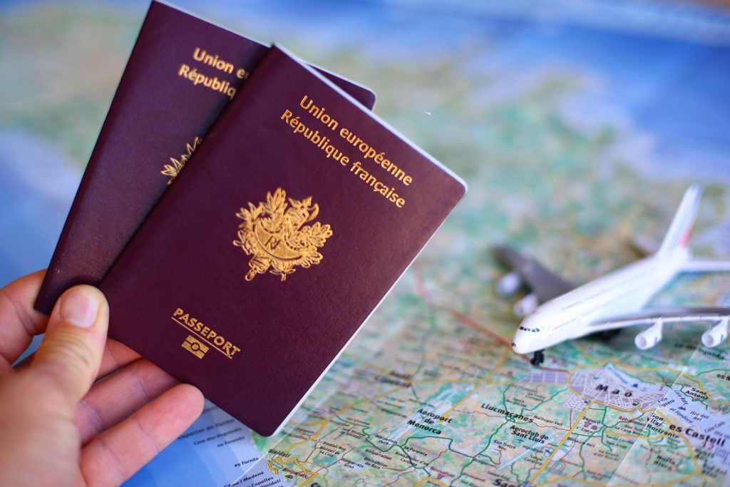 Mão segurando passaportes com mapa e avião miniatura ao fundo