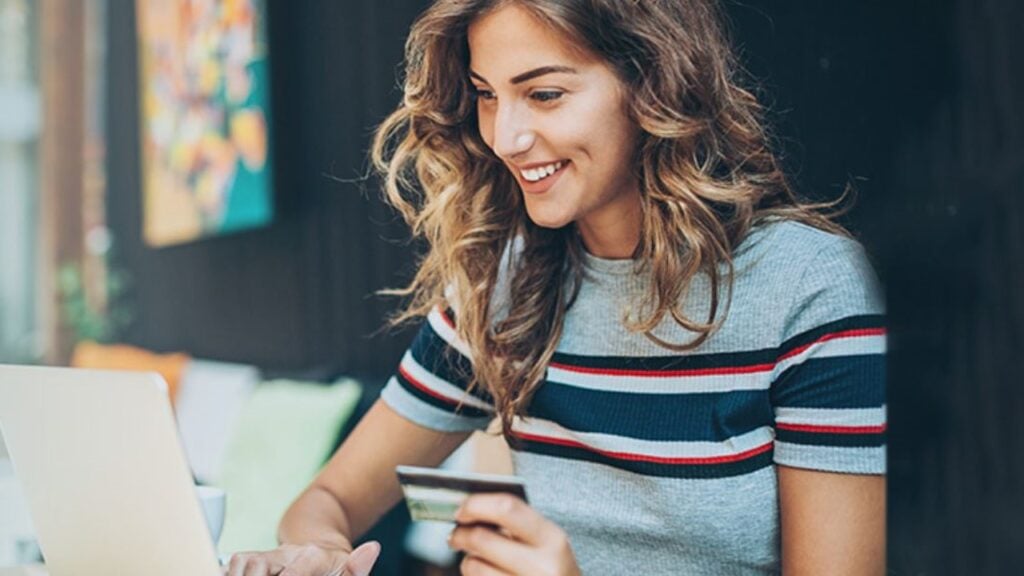 Mulher sorrindo segurando cartão e olhando notebook